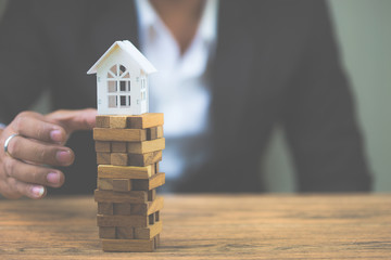 Businessman hand holding model white house on wood block. Investment risk and uncertainty in the real estate housing market. Property investment and house mortgage financial concept. with copy space