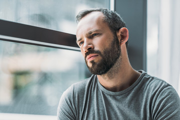 frustrated bearded man leaning at window and looking away