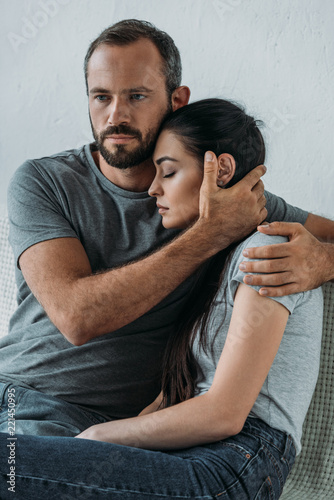 Fotografía bearded man supporting and hugging stressed sad woman sitting on couch