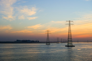 High voltage Electricty Power lines distributed through Ocean with amazing colourful clouds in background