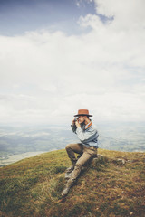 Wall Mural - travel and wanderlust concept. stylish traveler man sitting on top of  mountains with photo camera in clouds. space for text. hipster guy traveling, taking images. amazing atmospheric moment.