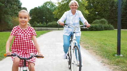 Sticker - family, leisure and people concept - happy grandmother and granddaughter riding bicycles at summer park