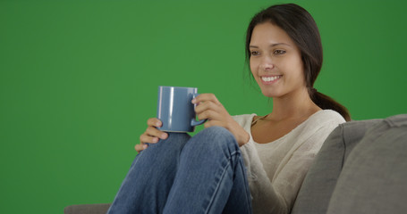 Wall Mural - Portrait of millennial girl sitting on couch drinking coffee on green screen