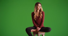 Attractive Woman Sitting On Stool Looking Offscreen Smiling On Green Screen