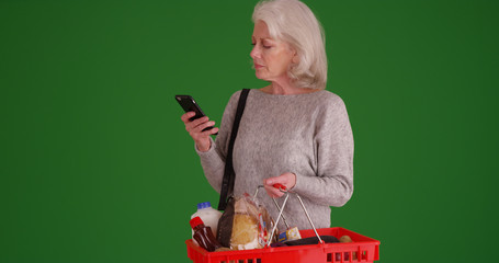 Wall Mural - Old white woman out grocery shopping using phone on green screen