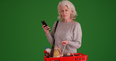 Wall Mural - Old lady searching nutrition facts on phone while out shopping on green screen