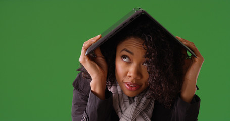 Poster - Young black female covering head from rain with laptop on green screen