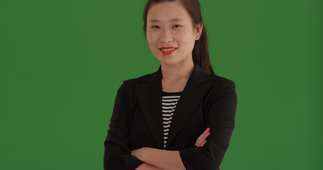 Charming Asian business lady smiling with arms crossed on green screen