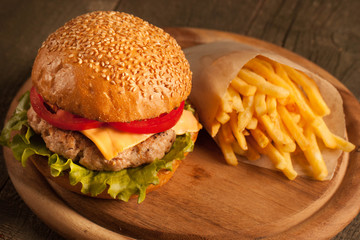 Home made hamburger with beef, onion, tomato, lettuce and cheese. Fresh burger close up on wooden rustic table with potato fries, beer and chips. Cheeseburger.