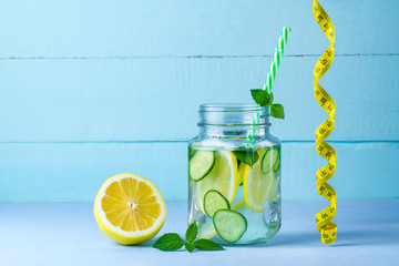 Wall Mural - Diet concept. Detox drinks. Lemon water, juicy lemon, mint and measuring tape on a blue background.