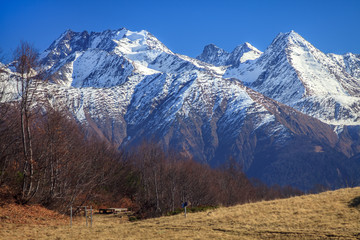 Wall Mural - Beautiful scenic blue sky sunny autumn landscape of snowy Main Caucasus Ridge in Caucasus Nature Reserve in Krasnaya Polyana, Sochi, Russia. Pseashkho mountain peaks on background