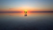 A young couple walking on calm mirrored surface of shallow water into the setting sun.. They are holding each other's hands