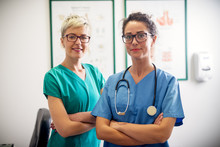 Portrait Of Two Professional Nurses Standing In Their Office In Front Of A Camera.