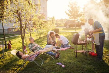 Big happy family enjoy making barbeque in their backyard on a sunny day.