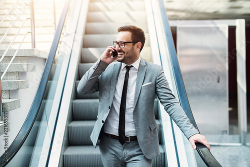 Fotomural Young modern successful businessman talking on the telephone while standing on a escalator