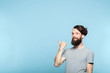 © golubovy - smiling man pointing behind his back to a virtual object or text. copy space for advertisement or product placement. portrait of a bearded hipster guy on blue background.