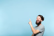 © golubovy - laughing man pointing behind sideways to a virtual object or text. copy space for advertisement or product placement. portrait of a bearded hipster guy on blue background.