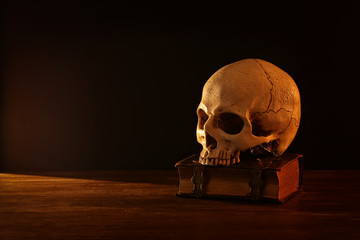 Human skull and old book over old wooden table and dark background.