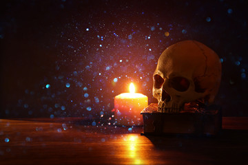 Wall Mural - Human skull, old book and burning candle over old wooden table and darl background.