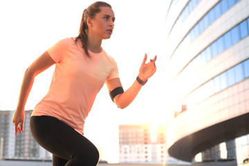 Young attractive sporty fitness woman running while exercising outdoors at sunset or sunrise in city.