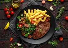 Grilled Sirloin Steak With Potato Fries And Vegetables, Tomato Salad In A Black Plate. Rustic Table