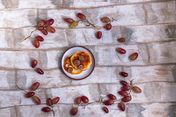 Background under the brickwork with a frame of ripe grapes and cheese cakes in the middle of the frame