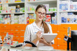© Leika production - A beautiful thin dark-haired girl with glasses,dressed in a lab coat,writes notes in a notebook at the cash desk in a modern pharmacy.