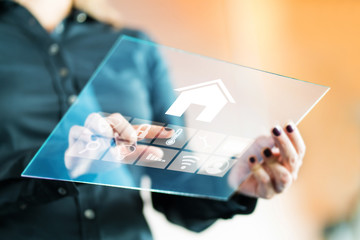 Woman using smart home control application with futuristic transparent glass tablet. Finger touching button to control property with automated digital technology, AI and IOT. Future of house tech.