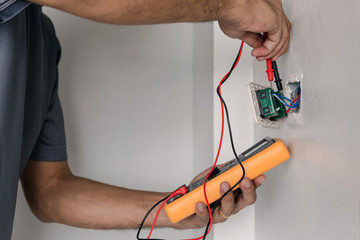 Electrician is using a digital meter to measure the voltage at the power outlet in on the wall.