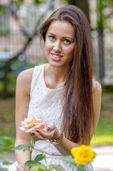 Young girl in a white dress in a summer park smelling a rose
