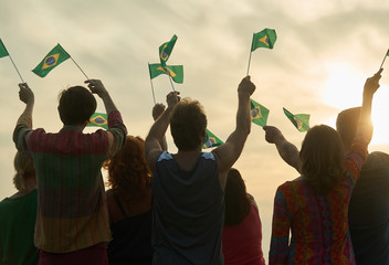 Wall Mural - Group of people waving brazilian flags. Brazil family against evening sky background.