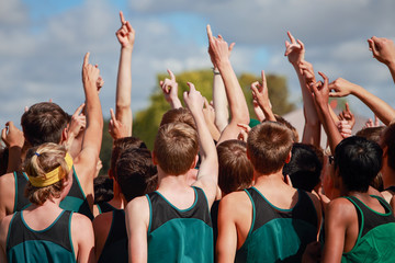 Boys on cross country team in a huddle raising arms pointing their fingers for number one