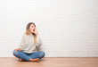 © Krakenimages.com - Young adult woman sitting on the floor over white brick wall at home shouting and screaming loud to side with hand on mouth. Communication concept.