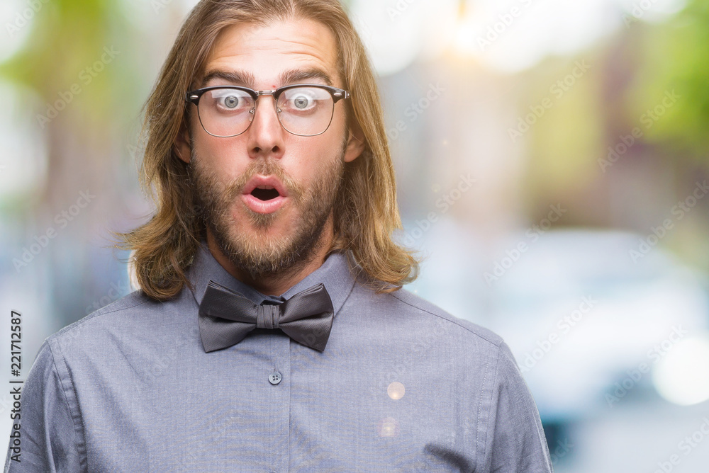 Young handsome man with long hair wearing bow tie over isolated background afraid and shocked with surprise expression, fear and excited face.