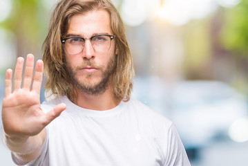 Poster - Young handsome man with long hair wearing glasses over isolated background doing stop sing with palm of the hand. Warning expression with negative and serious gesture on the face.