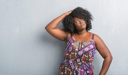 Wall Mural - Young african american woman over grey grunge wall wearing colorful dress confuse and wonder about question. Uncertain with doubt, thinking with hand on head. Pensive concept.