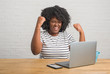 © Krakenimages.com - Young african american woman sitting on the table using computer laptop screaming proud and celebrating victory and success very excited, cheering emotion