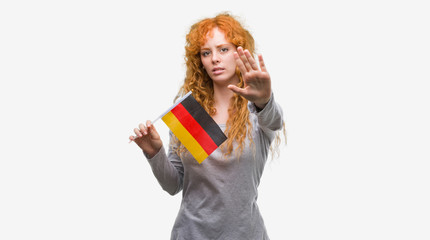 Sticker - Young redhead woman holding flag of Germany with open hand doing stop sign with serious and confident expression, defense gesture