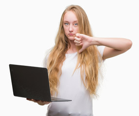 Sticker - Blonde teenager woman using computer laptop with angry face, negative sign showing dislike with thumbs down, rejection concept