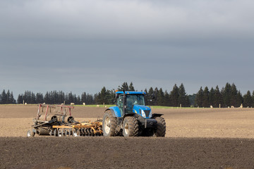 A blue tractor and plough on a ploughed field on a farm in New Zealand