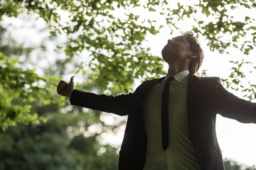 Wall Mural - Young peaceful businessman standing in spring forest looking upwards