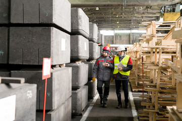 full length portrait of mature foreman wearing hardhat discussing manufacturing with worker while wa