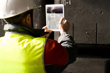 Back view portrait of modern factory worker wearing hardhat taking photo of codes while using digital tablet, copy space