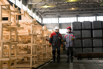 Full length portrait of two factory workers talking while walking towards camera in industrial workshop, copy pace