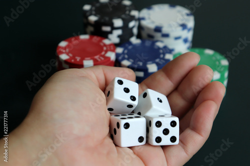 фотография A woman's hand holding dice with a pile of casinos chips.