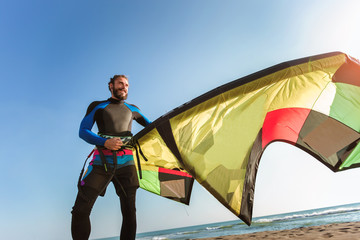 Handsome Caucasian man professional surfer standing on the sandy beach with his kite