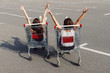 Back view of two woman sitting in shopping trolley cart on the parking