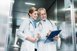 © LIGHTFIELD STUDIOS - happy mature male doctor showing clipboard to female colleague with digital tablet in hospital elevator