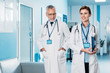 © LIGHTFIELD STUDIOS - happy female and male doctors with badges and stethoscopes over neck walking in hospital corridor