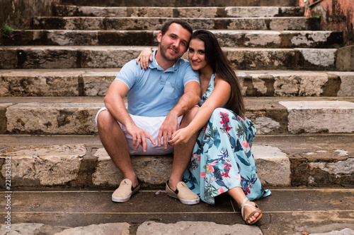 Fotografie, Obraz embracing couple sitting on the stairs looking at the camera.